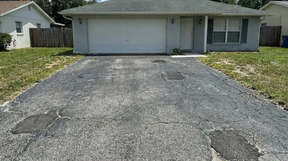 Worn asphalt driveway with patched potholes in front of a gray stucco home