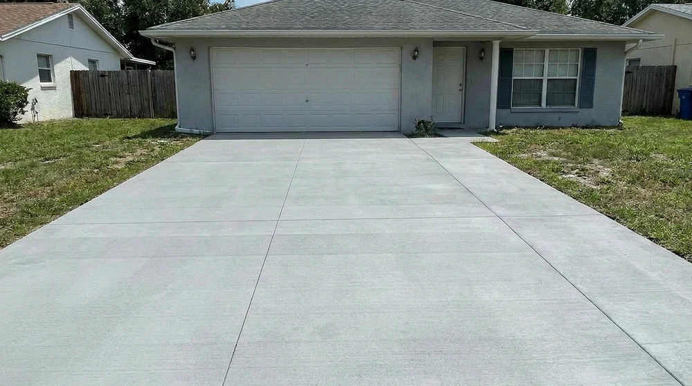 Smooth light gray concrete driveway in front of a single story house with a two car garage