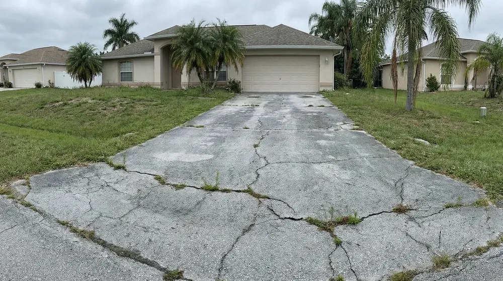 Cracked concrete driveway with weeds growing in the cracks, before replacement